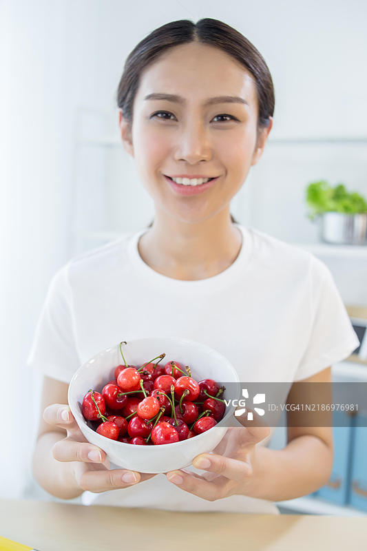 快乐的年轻女性手里拿着一碗新鲜的樱桃图片素材