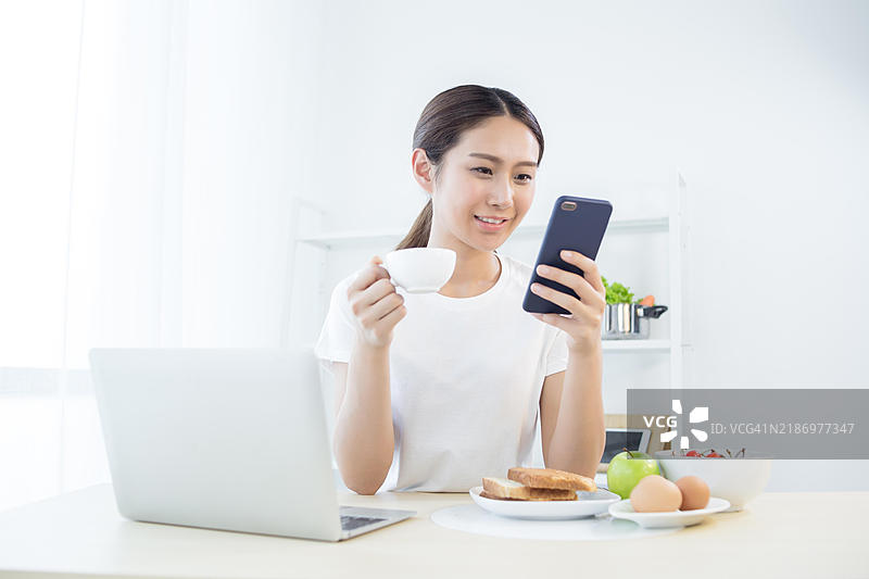 一位年轻女性在吃早餐时使用手机图片素材