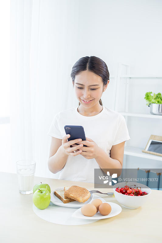 亚洲女性在吃早餐时使用智能手机图片素材