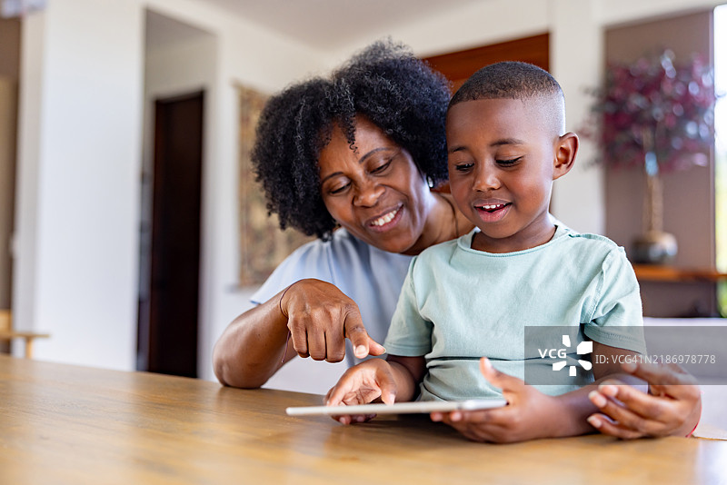 祖母在照看孙子，并使用平板电脑进行娱乐。图片素材