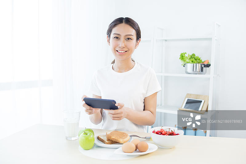 亚洲女性在吃早餐时使用智能手机图片素材