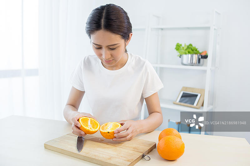 亚洲女性在厨房切橙子图片素材