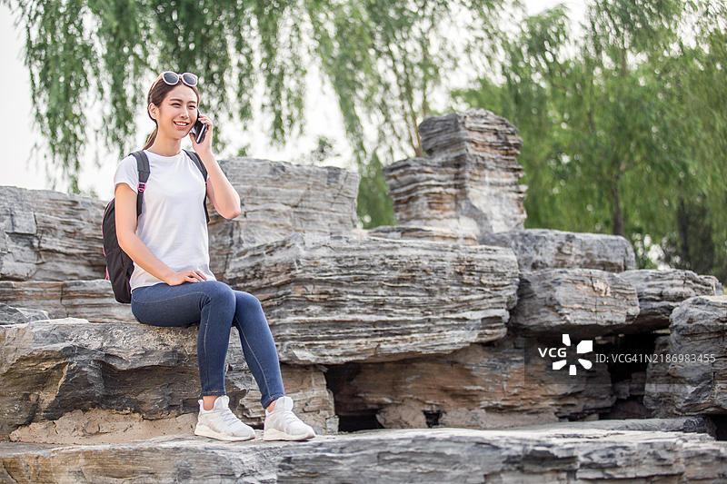 年轻女性坐在岩石上打电话图片素材