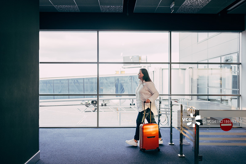 一位女性在机场走过，拖着一只明亮的橙色行李箱。图片素材