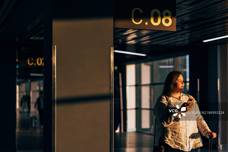 在金色时光的光线下，机场登机口的女人手持手机图片素材