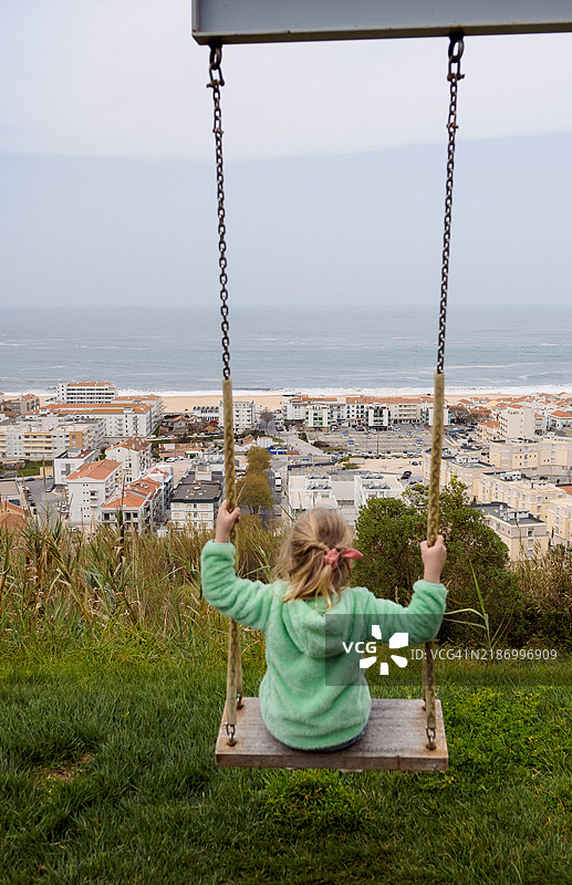 女孩坐在秋千上背对大海的侧面视图图片素材
