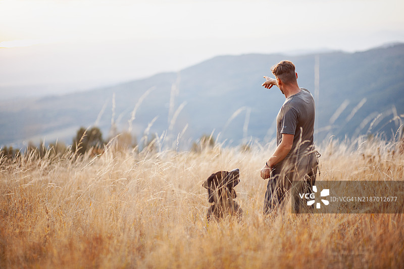 帅气的男人与他的狗在保加利亚的日落田野中探索大自然图片素材