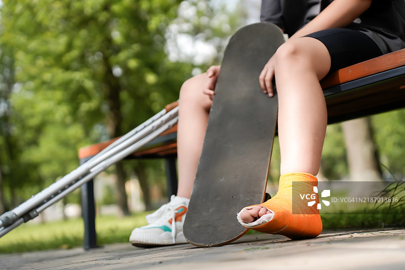 女孩的腿上绑着绷带，穿着橙色石膏，手里拿着滑板，留有空白以便于模版使用，去个性化处理。图片素材