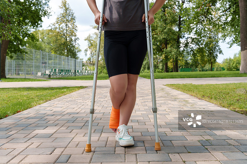 一位身份不明的女性身处公园环境，受伤的手臂用拐杖支撑。图片素材
