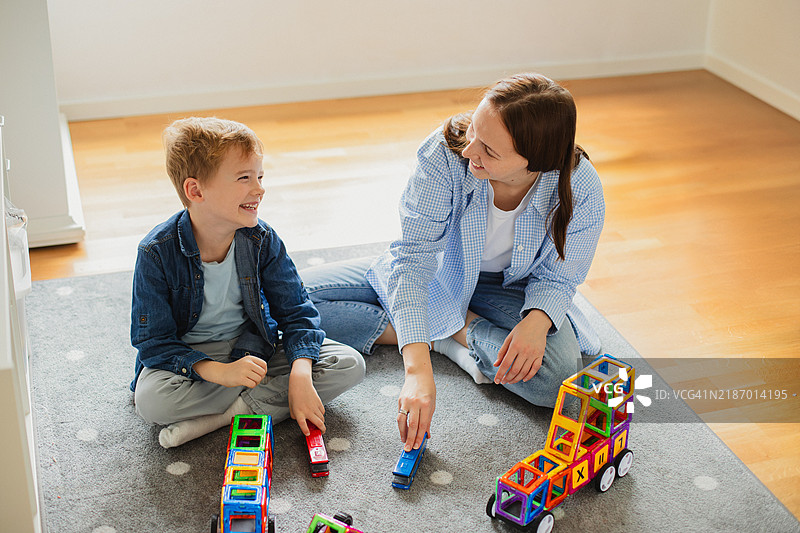 快乐的母亲和儿子在玩玩具车和彩色磁性积木，分享愉快的时光图片素材