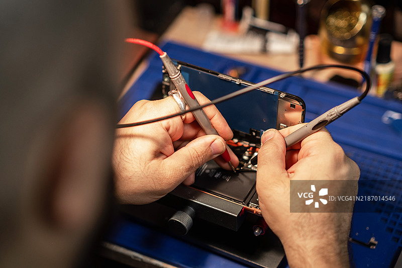 技术人员在工作坊中使用精密工具和设备进行智能手机电池维修图片素材