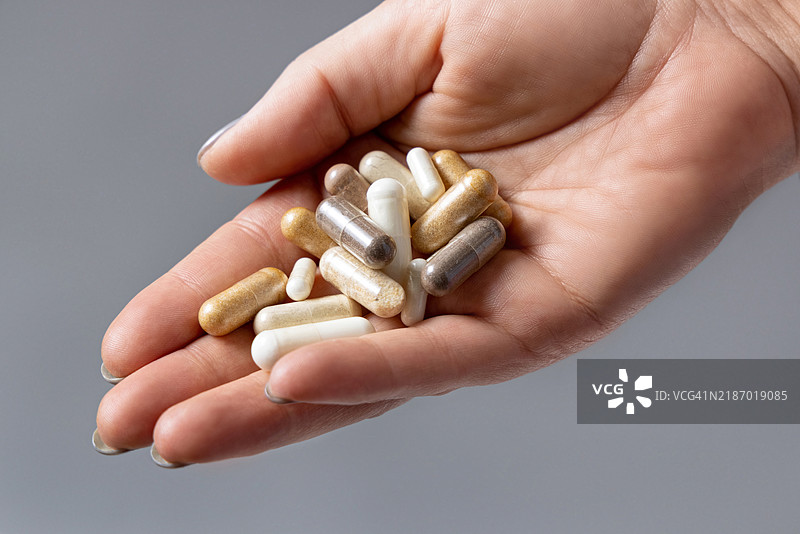 女人的手掌捧着一堆米色胶囊，特写在灰色背景上图片素材