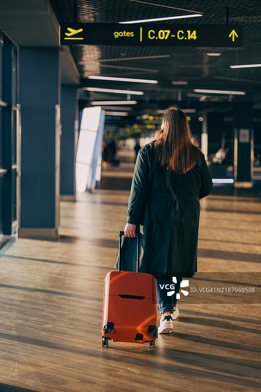 旅客拖着橙色行李箱走过机场航站楼图片素材