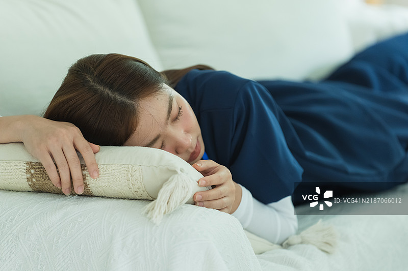 平静的亚洲女性护士在舒适的家中沙发上休息。图片素材