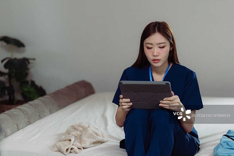 穿着医护服的工作人员坐在床上使用平板电脑。图片素材