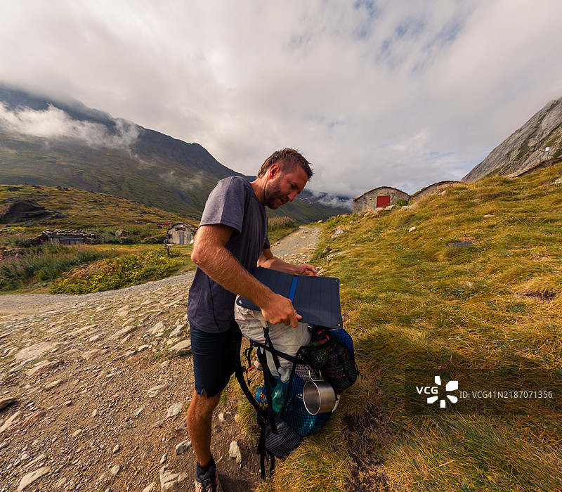 男子在崎岖的山地小径上整理背包图片素材
