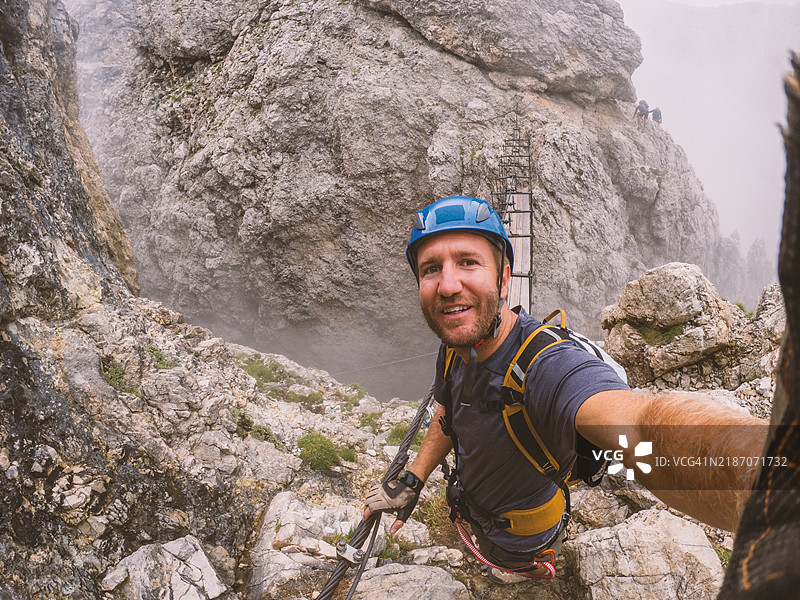戴着头盔和装备的男子攀爬岩石山路图片素材