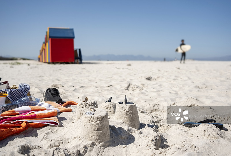 沙滩上的沙堡，旁边有毛巾、野餐篮和鞋子图片素材