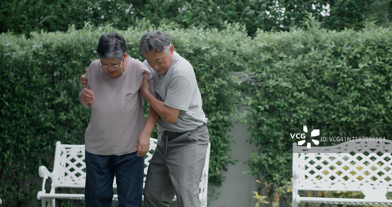 一位老人正在花园里伤到膝盖，我的妻子帮助我走路。图片素材