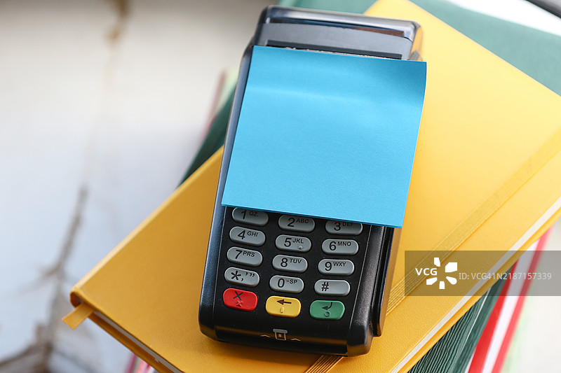 蓝色粘性贴纸贴在收银机上，背景是书籍和日记的堆叠。图片素材