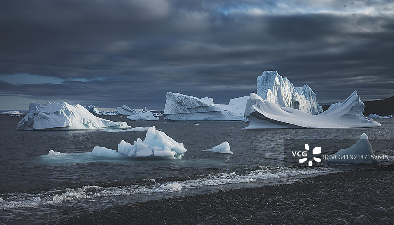 在阴郁的天空下，冰山漂浮在广阔的水域中，景色令人叹为观止。图片素材