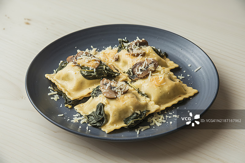 一盘装有煮菠菜的饺子，上面淋有奶油酱。图片素材