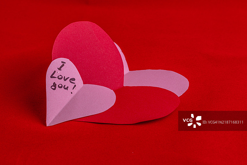用纸剪出的心形，上面写着“我爱你”，献给情人节图片素材