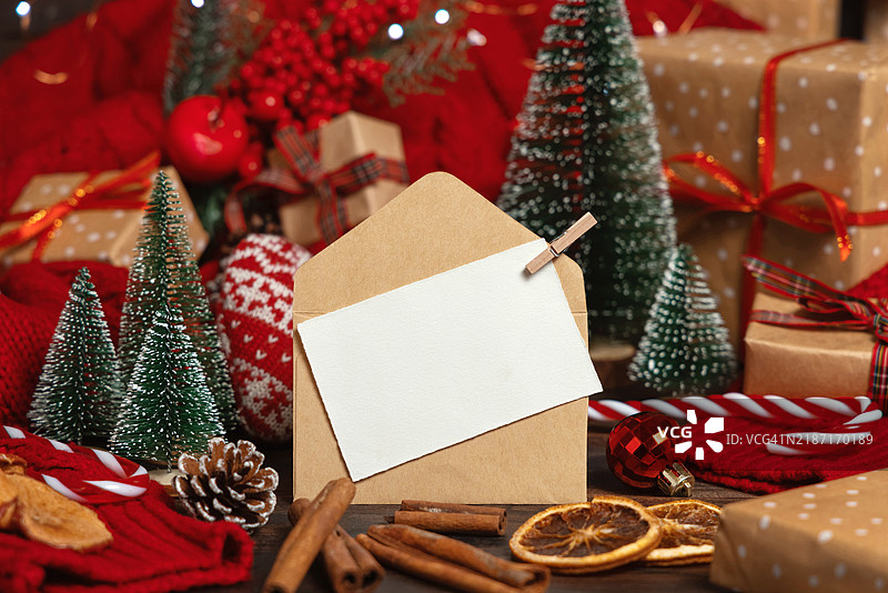 白色明信片和手工信封靠近圣诞装饰、树木、香料和红色毛衣，样机展示图片素材