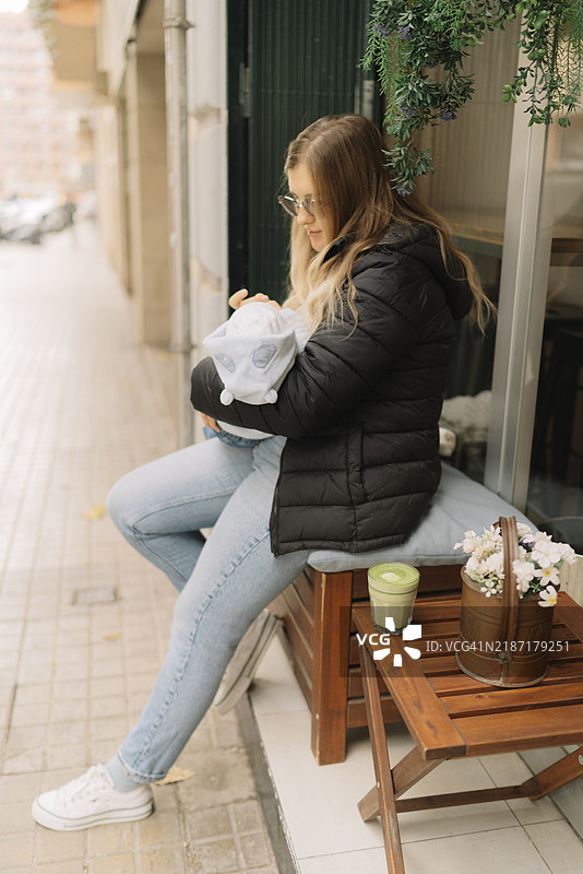 年轻女性戴着太阳镜，抱着婴儿坐在户外。图片素材