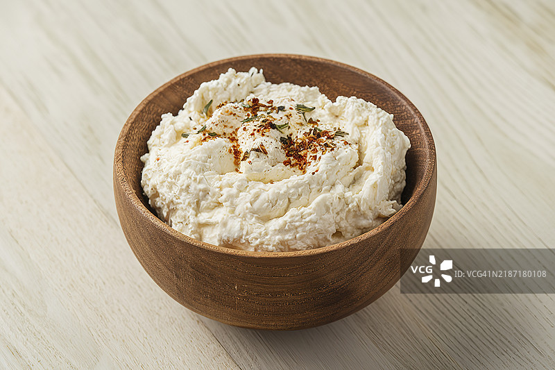 一个中景镜头，展示一个装满颗粒状白色里科塔奶酪的木碗。图片素材