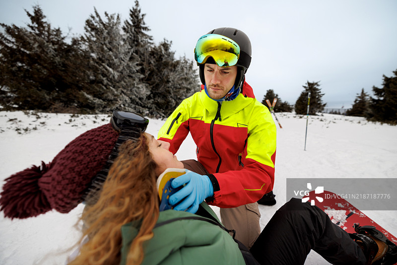 年轻的救援人员正在帮助一名受伤的年轻滑雪者，为她戴上颈托。图片素材
