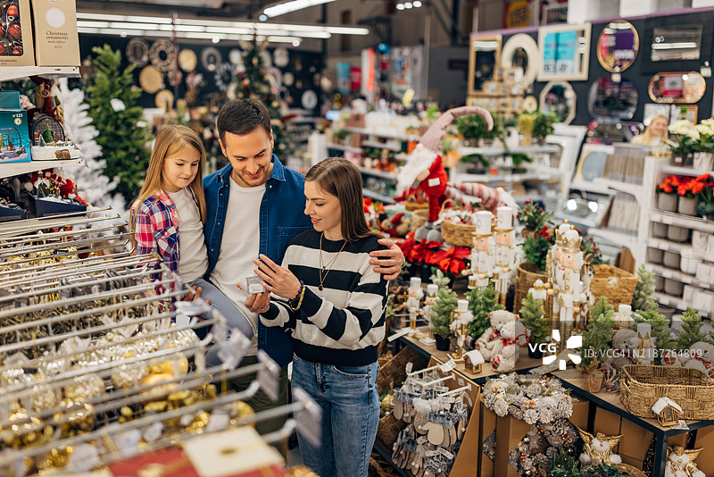 一个男人抱着女儿，搂着妻子，一起欣赏百货商店里的圣诞装饰。图片素材