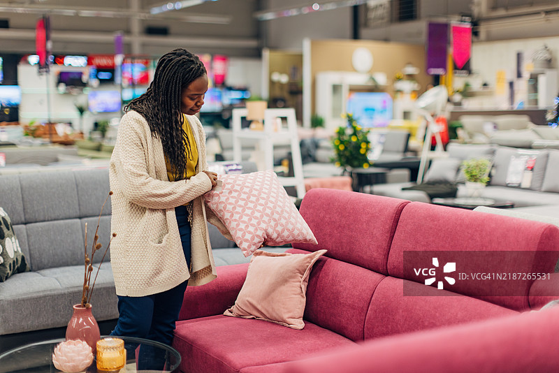 这位黑人女性正在百货商店的沙发床和枕头展示区。她正在为她的新客厅挑选家具和枕头。图片素材