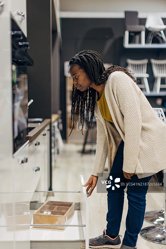 一位穿着休闲服的黑人女性在家具店查看厨房，以便为她的新公寓购买。她打开抽屉查看存储空间有多少。图片素材