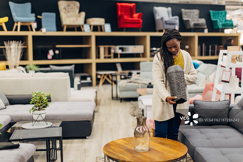 一位无忧无虑的黑人女性在百货商店里欣赏展示的家具。她正在寻找可以美化她居住空间的漂亮花瓶。图片素材