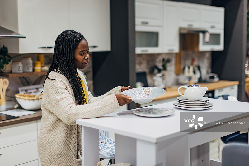 一位穿着休闲服的女性在百货商店购买餐具。她正在挑选要购买的餐具。图片素材
