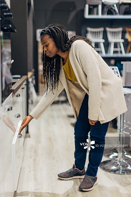 一位黑人女性在百货商店里观看各种类型的现代厨房展示。图片素材