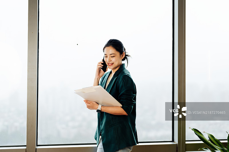 自信的亚洲女商人在现代办公室中。她正在使用手机并查看案例。女性投资者和财务顾问的成功。图片素材