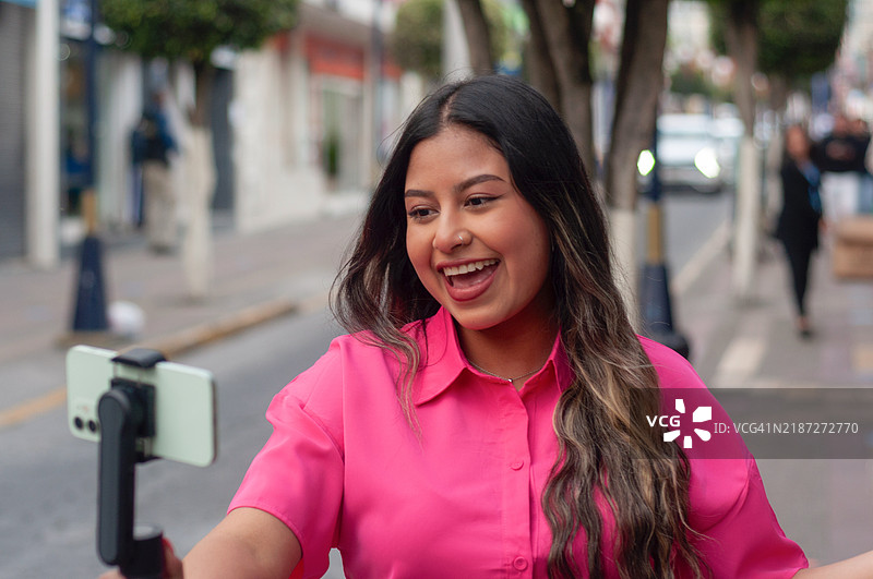 年轻女性在繁忙的城市街道上用智能手机录制视频并微笑。世界旅游日图片素材