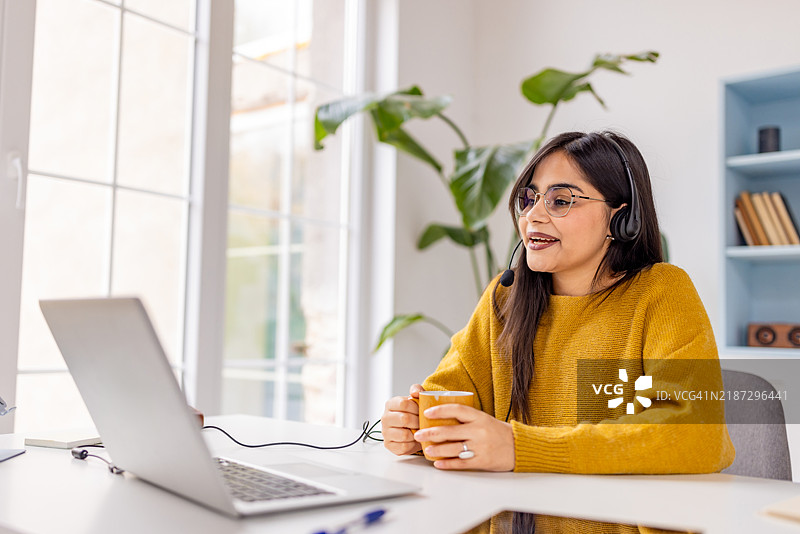 在明亮的环境中，戴着耳机的已订婚女性在家工作。图片素材