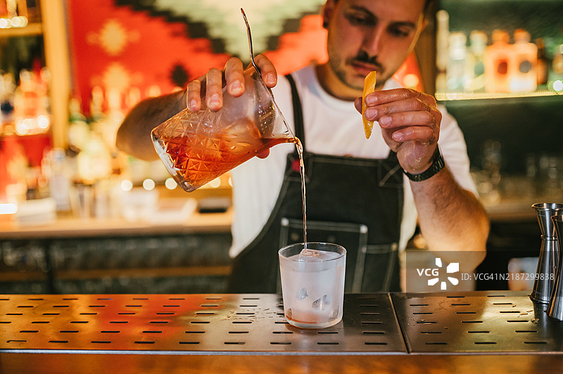 男性调酒师正在准备橙皮尼格罗尼鸡尾酒。图片素材