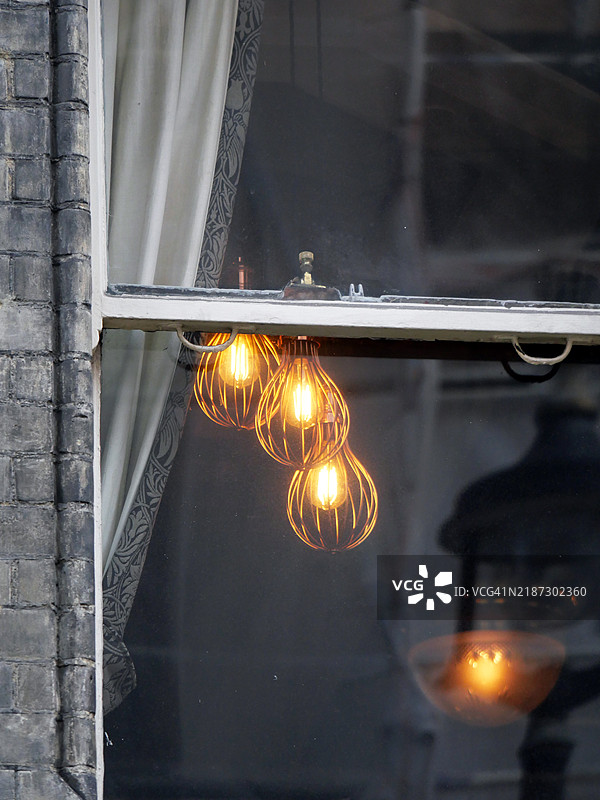 透过窗户看到的点亮的灯具特写。灰色和风化的砖墙。阳光。自然色彩。伦敦，英格兰，联合王国。图片素材