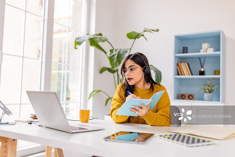 戴着耳机的女性在视频通话中做笔记图片素材