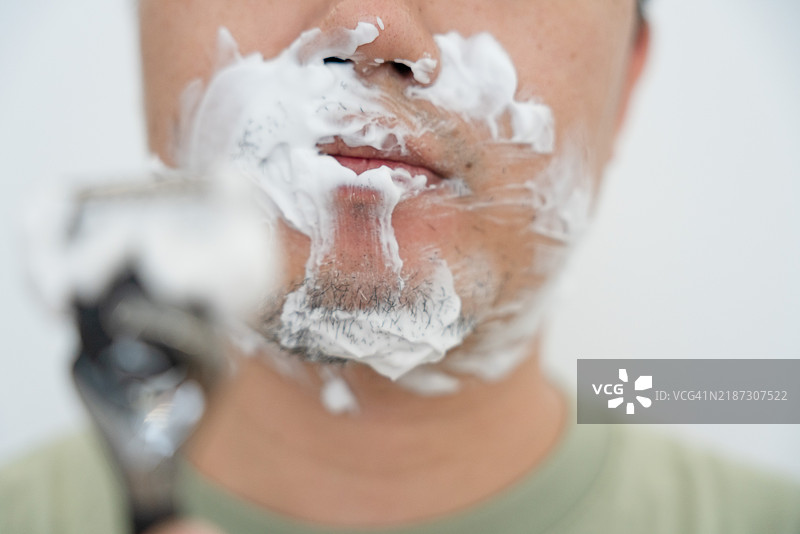 一位亚洲男性正在刮胡子；使用剃须泡沫刮胡子图片素材
