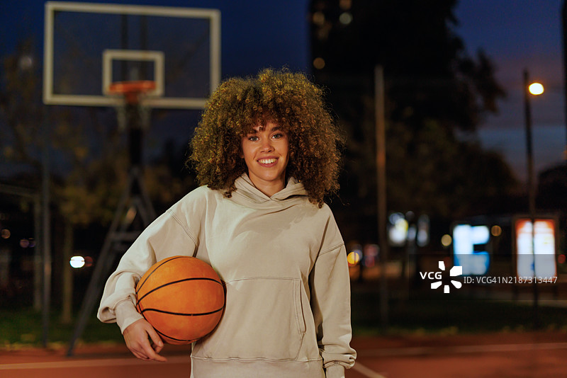 年轻女子在户外篮球场上站着，傍晚时分图片素材