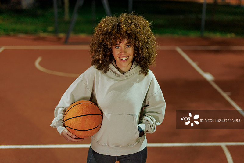 微笑的女性在黄昏时分的篮球场上拿着篮球图片素材