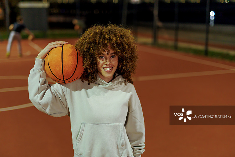 自信的女性在明亮的篮球场上持球图片素材