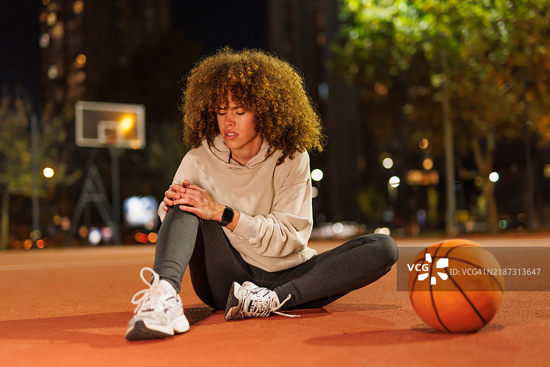 一位穿着黑色运动服的年轻女性在篮球场上受伤了膝盖。图片素材
