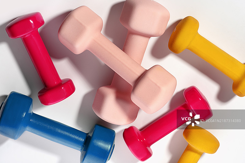 由红色、粉色、蓝色、黄色和橙色哑铃组成的运动图案，背景为白色。特写，健康生活方式、运动、普拉提、健康俱乐部的概念。图片素材