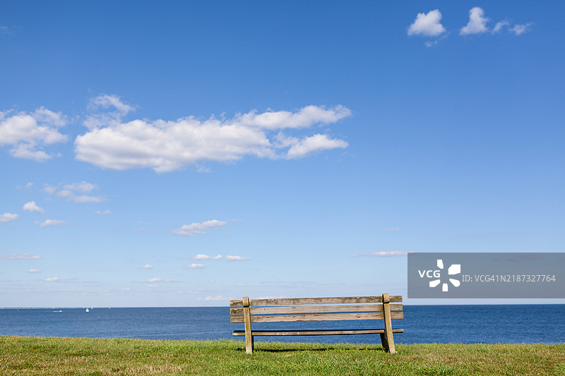 草地上的旧木长椅，面朝大海。图片素材